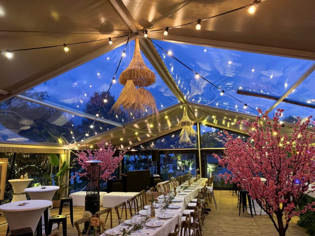 Feestelijk ingerichte binnenzijde van een transparante aluhal met verlichting en decoratie.