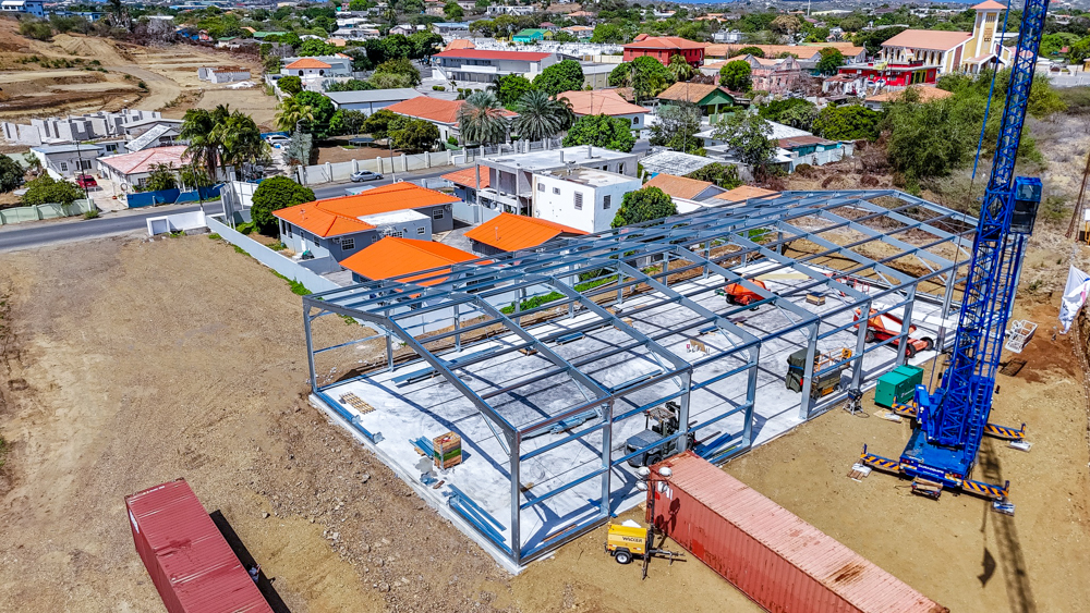 Opbouw van het stalen frame van de Flexhal in Curaçao, met oranje daken op de achtergrond